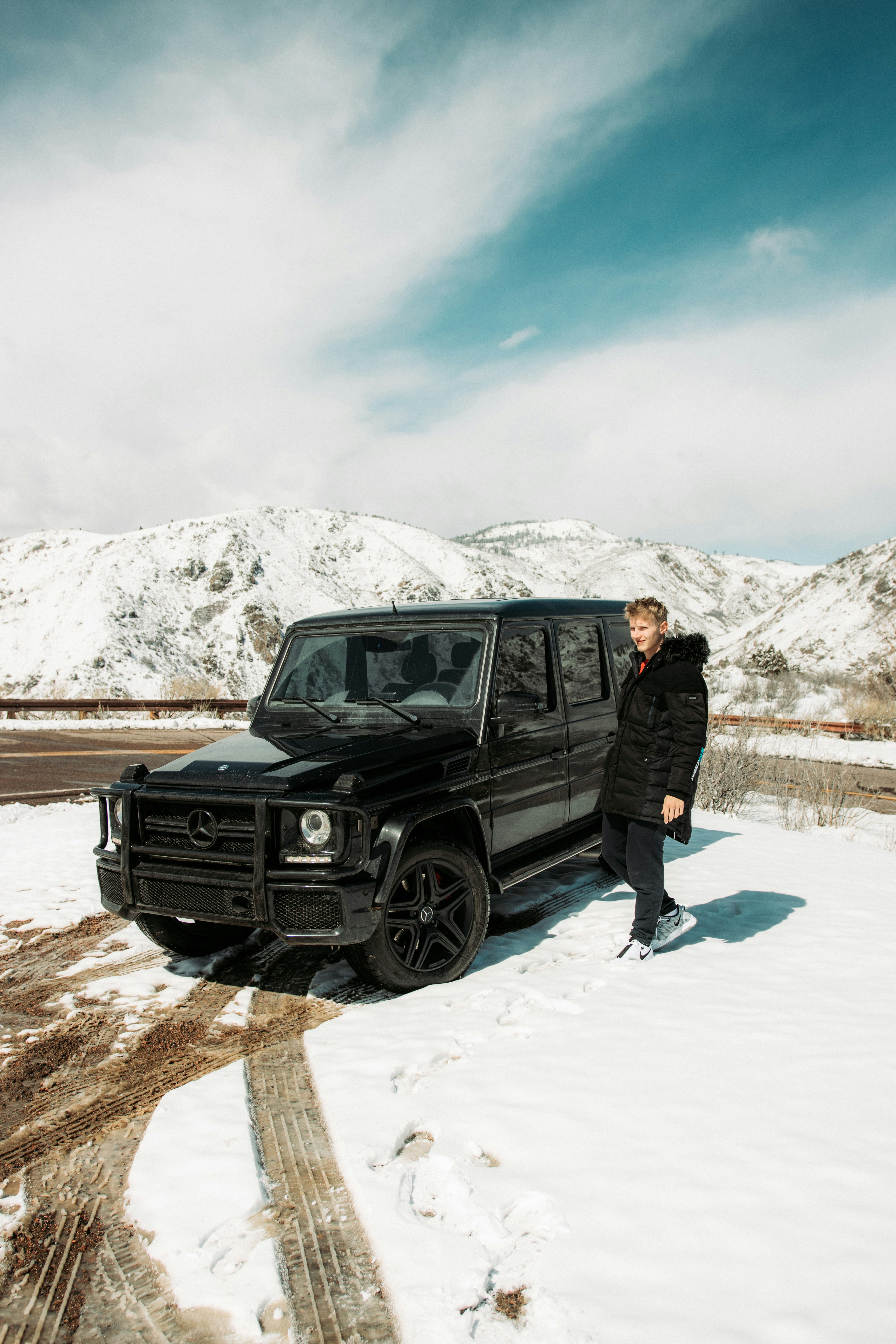 man in black jacket standing beside black suv during daytime